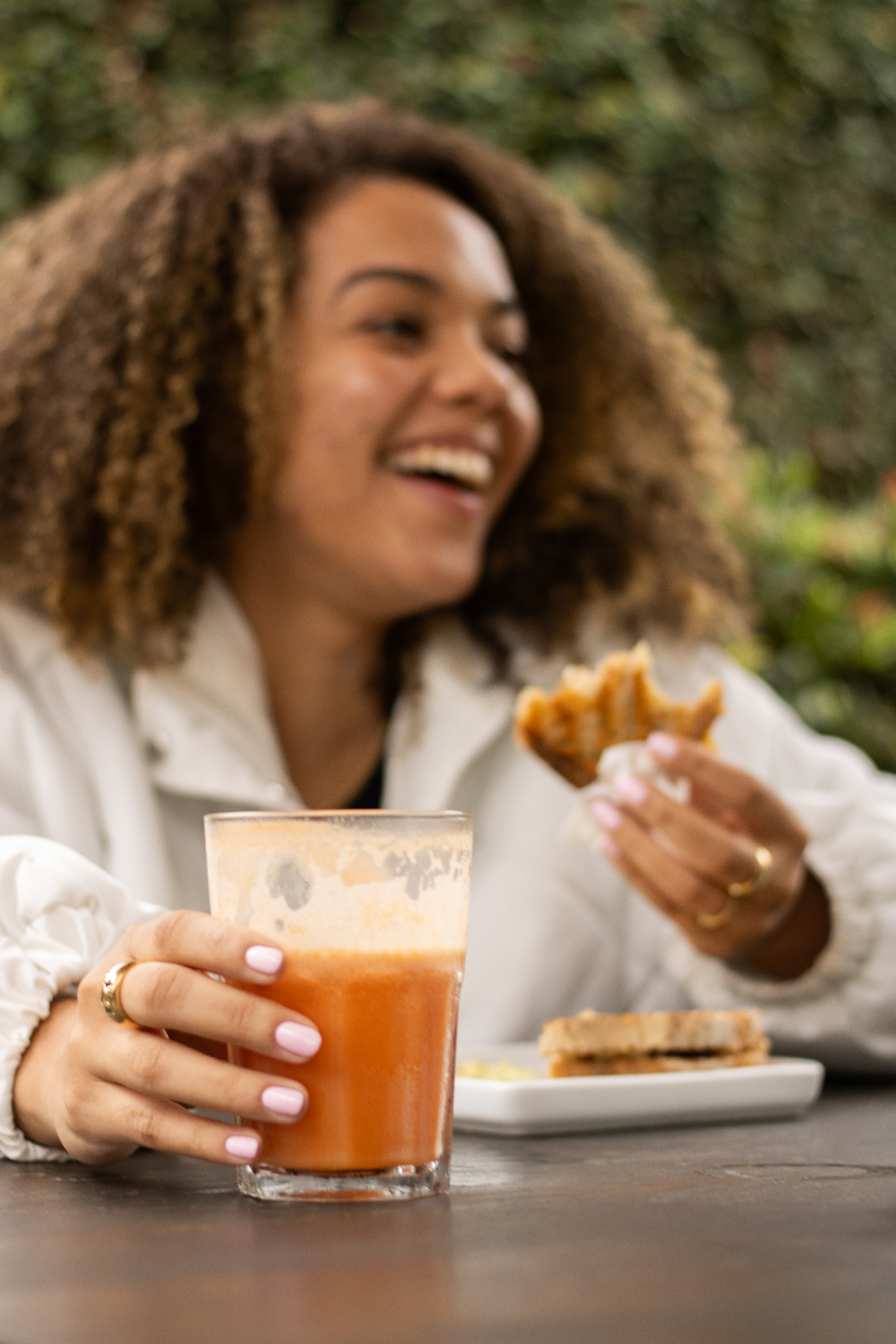 Cliente sorrindo na área externa do Yarn, com copo de suco e sanduíche.